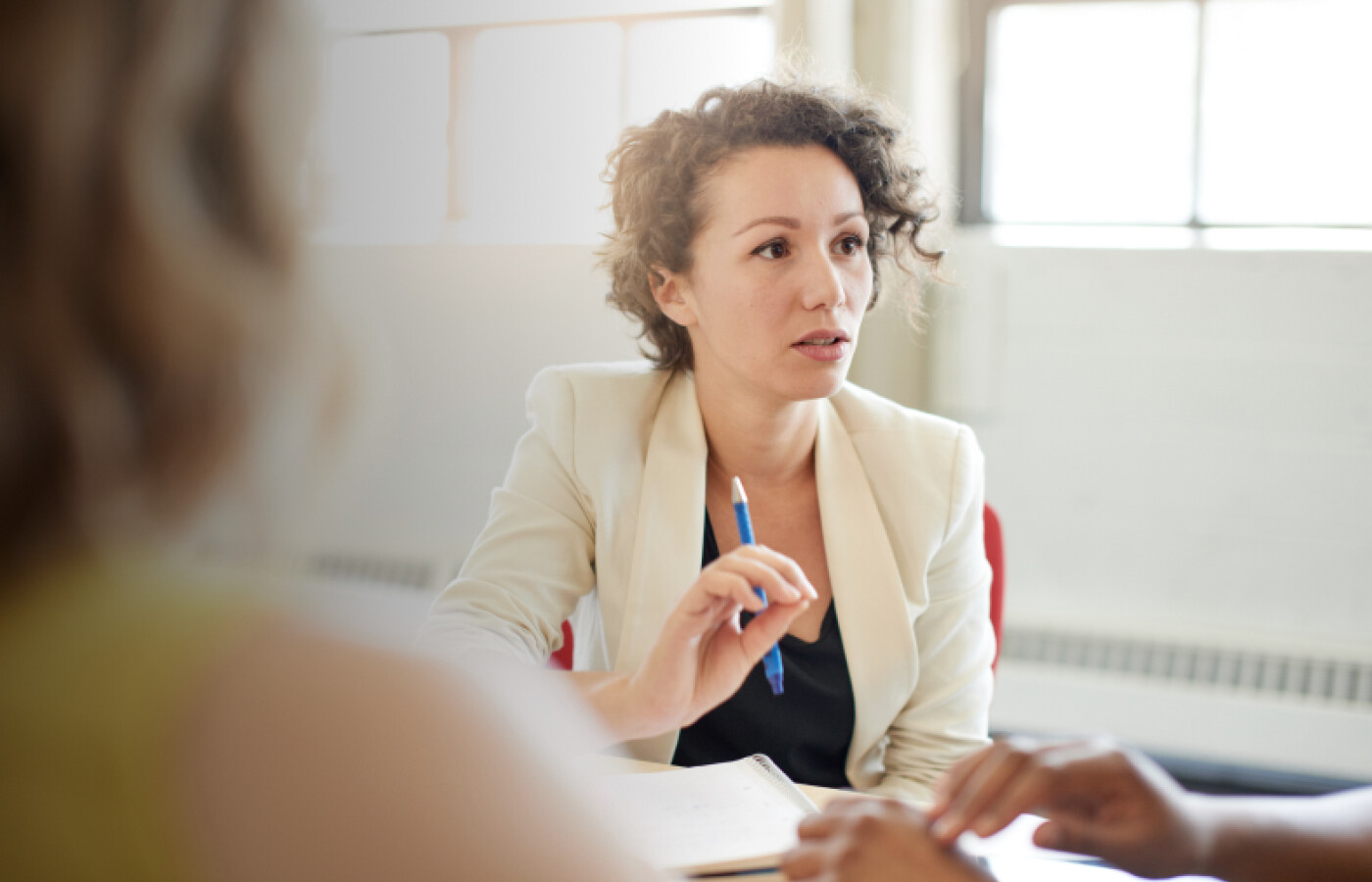 Woman in a blazer holding a pen and speaking to people outside the frame